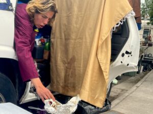 Person leans from the back seat of a car at Hawthorne and Pine behind the Poverello Center to adjust cooking foil on portable camping burner.