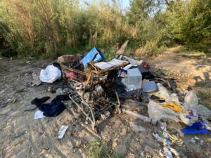 A shopping cart filled with trash surrounded by more trash near the Clark Fork River waterfront